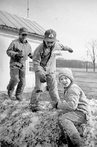 Three boys playing on a mound of snow